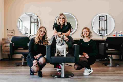 Das Team der Haarmanufaktur Suszan mit Salonhund vor drei runden Spiegeln im Friseursalon